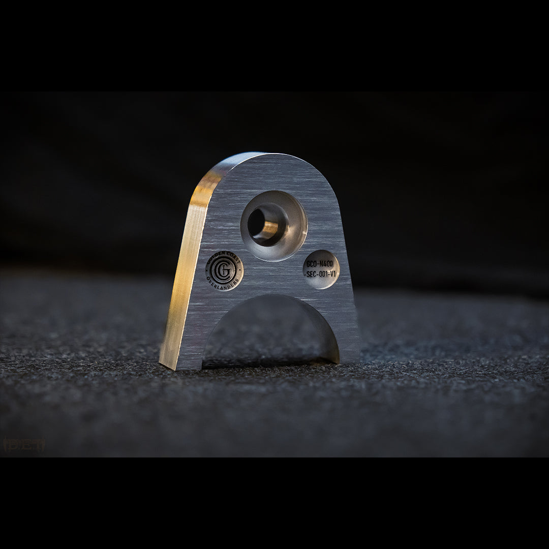 Close-up of CNC machined 6061-T6 billet aluminum tailgate lock for 2024+ Toyota Tacoma. Shows brushed surface finish and laser engraving.